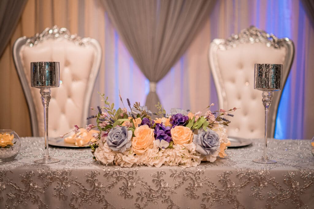 sweetheart table with two large white upholstered chairs and floral arrangement